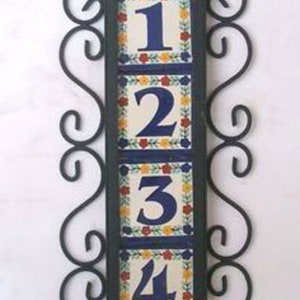 May include: A black metal frame with four colorful ceramic tiles, each with a white number, 1, 2, 3, and 4. The tiles are decorated with floral designs in yellow, red, and blue.
