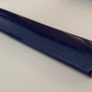 May include: A dark blue ceramic tile trim piece with a rounded edge and a beveled corner. The tile is glazed and has a smooth, glossy finish.