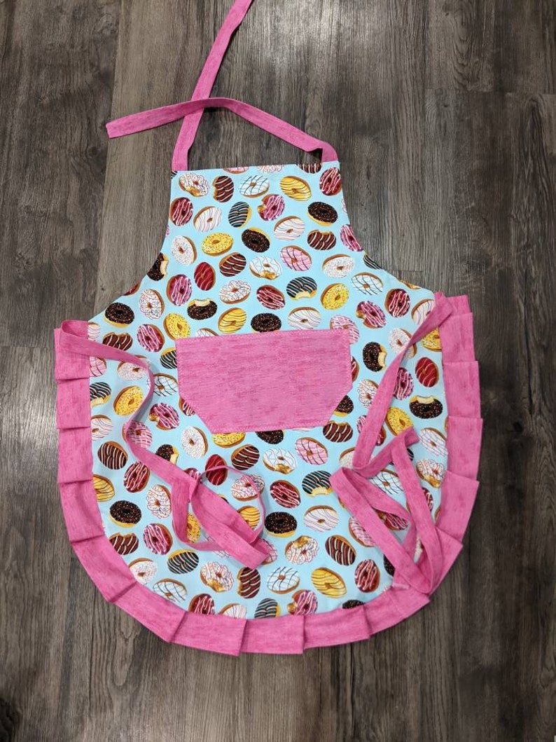 Multi-colored frostedsprinkled donuts on main Bright pink and pocket ties and frills. Women/'s apron Adult apron