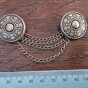May include: A silver chain with two decorative round pendants. Each pendant has a circular design with a floral pattern.