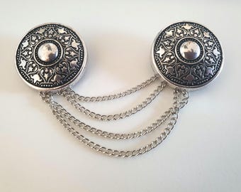 May include: A silver chain with two decorative round pendants. Each pendant has a black and silver design with intricate details.