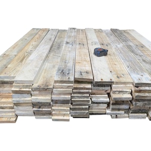 May include: A pile of reclaimed wooden planks in shades of grey and beige, showing visible grain and texture. A measuring tape sits on top of the planks. Suitable for rustic decor or DIY projects.