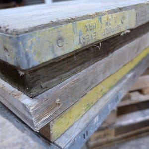 May include: Close-up of a stack of wooden planks with metal banding. The top plank has a yellow painted metal tag with the text "SUPPORT EVERY HX 121 C".