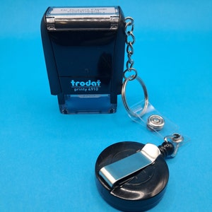 May include: Black self-inking stamp with a silver chain and a retractable badge holder. The stamp reads "trodat printy 4910" and has a white label that says "Dr. Robert Fleck Consultant".