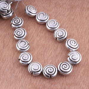 May include: A strand of silver-toned metal beads with a spiral design. The beads are round and have a smooth, polished finish.