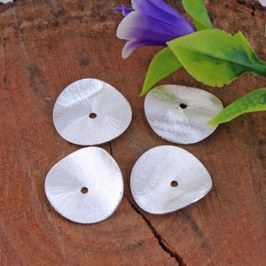 May include: Four silver-colored metal flower-shaped embellishments with a hole in the center. The embellishments are on a wooden surface.