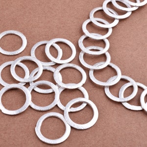 以下が含まれることがあります： 銀色の金属製のリングの山をクローズアップした写真。リングはすべてサイズが異なり、ランダムなパターンで配置されています。リングは滑らかで光沢があります。