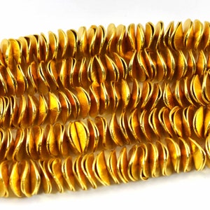 May include: A strand of gold-coloured metal beads, each bead is shaped like a half-circle with a wavy edge.