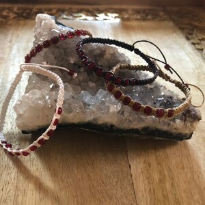 May include: Four bracelets with red beads and white, black, and brown string. The bracelets are displayed on a white crystal rock.