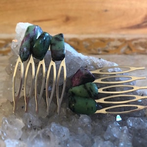 May include: A silver hair comb with five teeth decorated with green and pink gemstones.