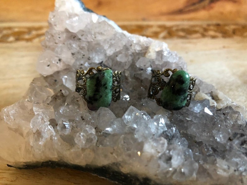 May include: Two green gemstone rings with ornate gold settings. The rings are displayed on a bed of white crystals.