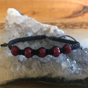 May include: A black cord bracelet with five dark red beads.