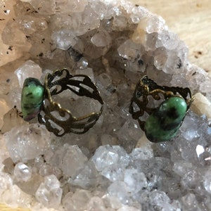 May include: Two rings with green and black gemstone settings. The rings are made of brass and have a filigree design.
