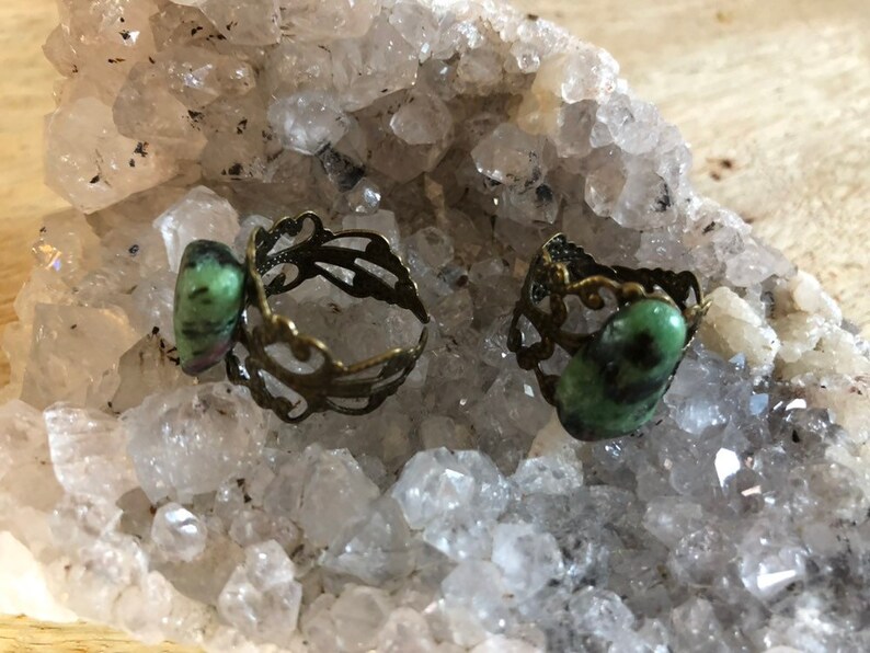 May include: Two rings with green and black gemstone settings. The rings are made of brass and have a filigree design.