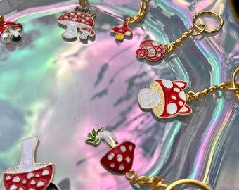 May include: A set of six gold keychains featuring red and white mushroom charms. The charms are enamel and have a 3D effect. The keychains are perfect for adding a touch of whimsy to your keys or bag.