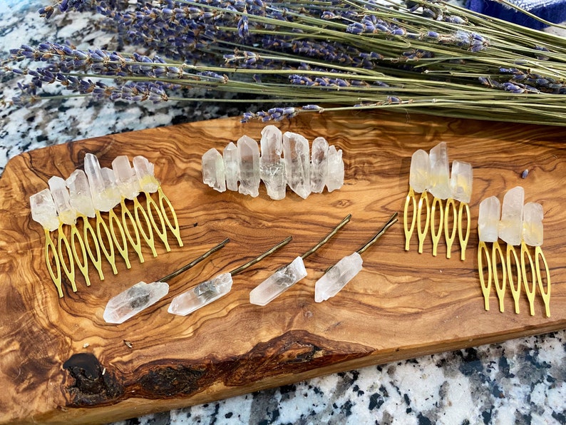 Op de afbeelding: Een set haar kammen en pinnen met heldere kwartskristallen. De kammen zijn goudkleurig en hebben een decoratief ontwerp. De pinnen zijn eenvoudig en recht. De kristallen zijn in verschillende maten en vormen.