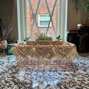 May include: A copper wire storage basket with a woven macrame trim. The basket is sitting on a granite countertop.