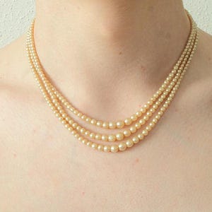 Puede incluir: Un collar de perlas de tres hilos con un suave color crema. El collar est&aacute; compuesto por perlas graduadas, con las perlas m&aacute;s grandes en el centro y las m&aacute;s peque&ntilde;as hacia el cierre. Una joya cl&aacute;sica.