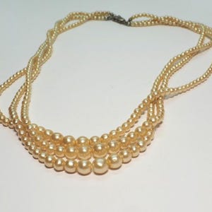 Puede incluir: Un collar vintage con tres hilos de perlas de imitaci&oacute;n de color crema. Los hilos est&aacute;n entrelazados en la parte superior y asegurados con un cierre plateado. El collar tiene un dise&ntilde;o cl&aacute;sico y elegante, perfecto para eventos.