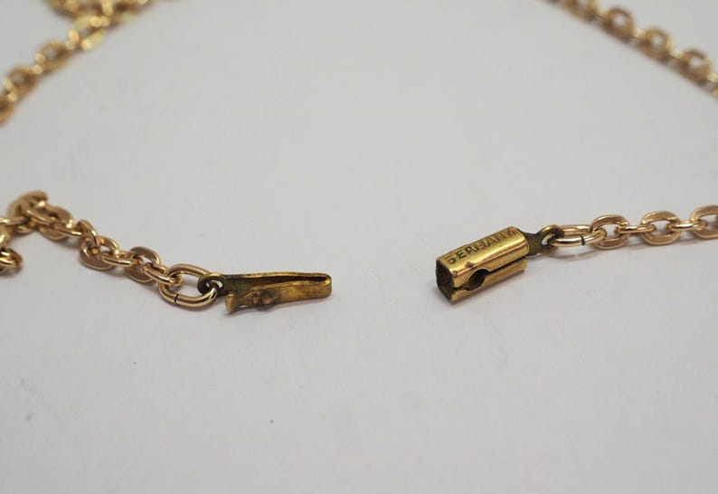 May include: Close-up of a gold-colored necklace with a chain link design. The clasp is open, revealing the intricate details of the chain and the clasp mechanism. The word "GERMANY" is visible on the clasp.