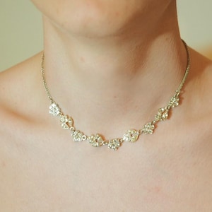 May include: A silver necklace with floral pendants, each set with clear crystals. The necklace is worn around the neck, highlighting its delicate design. The necklace's design is elegant and would suit a special occasion.