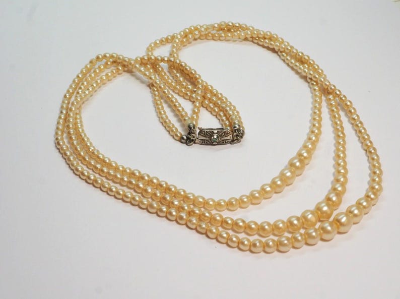 Puede incluir: Collar de tres hilos con perlas de imitaci&oacute;n de diferentes tama&ntilde;os, color crema. El cierre es plateado. Los hilos est&aacute;n dispuestos en cascada, creando un aspecto cl&aacute;sico y elegante. Una joya atemporal, perfecta para cualquier ocasi&oacute;n.