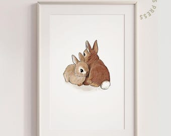May include: A framed print featuring a watercolor illustration of two brown rabbits. One rabbit is nestled against the other, with a white fluffy tail visible. The print is in a white frame and has the text "GREEN GABLES PRESS" in a circular design.