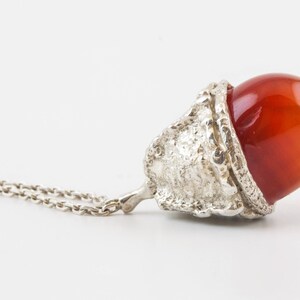 Op de afbeelding: Een zilveren ketting met een hanger van carneol. De hanger is gevormd als een eikel en heeft een getextureerde zilveren dop.