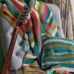 May include: A teal, gray, white, and mustard yellow striped crocheted throw blanket with tassels draped over a chair with a guitar.