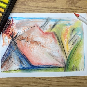 Op de afbeelding: Een abstracte pasteltekening op wit papier, met een bergachtige vorm in tinten oranje, rood en blauw. Een doos met kleurrijke pastels en een witte potlood met een rode punt liggen op een houten oppervlak. Er is ook een klein zwart blok pastels aanwezig.