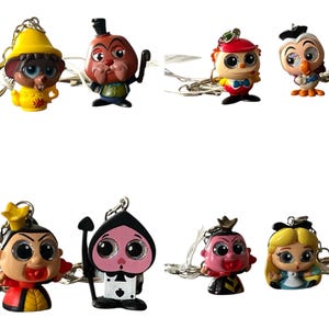 May include: Set of ten colorful cartoon character keychains featuring characters from Alice in Wonderland. The keychains are made of plastic and have large eyes. The characters include the Mad Hatter, the Queen of Hearts, the Cheshire Cat, the White Rabbit, and Alice.