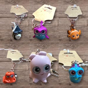May include: A collection of six keychains featuring colorful cartoon sea creatures. Each keychain has a silver-tone metal ring and a small, decorative tag. The creatures include a fish, a shark, and an octopus.