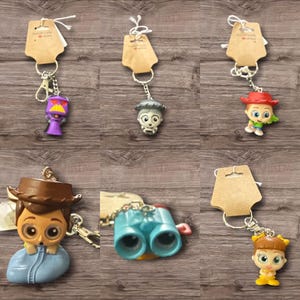 May include: A collection of character keychains, each attached to a metal keyring and a small brown tag. The keychains feature various cartoon figures in bright colors, including a purple robot, a skull, a cowboy, binoculars, and a girl.