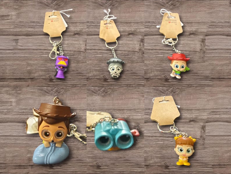 May include: A collection of character keychains, each attached to a metal keyring and a small brown tag. The keychains feature various cartoon figures in bright colors, including a purple robot, a skull, a cowboy, binoculars, and a girl.
