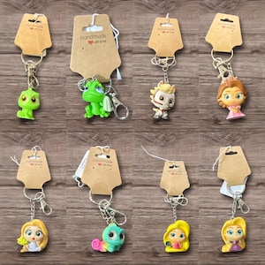May include: A collection of character keychains, each attached to a brown paper tag with the text "Handmade with love." The keychains feature various cartoon figures in vibrant colors, including a green dinosaur and a princess.
