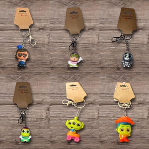Puede incluir: Una colecci&oacute;n de seis llaveros de personajes, cada uno unido a un llavero de metal y una etiqueta de papel marr&oacute;n. Los llaveros presentan varias figuras de dibujos animados en colores brillantes, incluyendo un robot y un extraterrestre.
