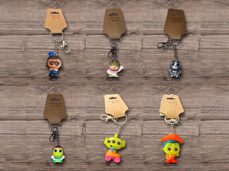 Puede incluir: Una colecci&oacute;n de seis llaveros de personajes, cada uno unido a un llavero de metal y una etiqueta de papel marr&oacute;n. Los llaveros presentan varias figuras de dibujos animados en colores brillantes, incluyendo un robot y un extraterrestre.