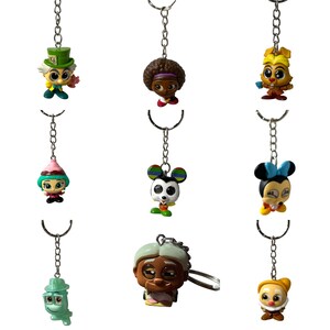 May include: Nine colorful character keychains with silver chains. The characters include a Mad Hatter, a girl with an afro, a bunny, a girl with a pink hat, a Mickey Mouse character, a Minnie Mouse character, a woman with gray hair, a green frog, and a clown.