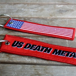 May include: Two red keychains with metal rings. The top keychain features an American flag design. The bottom keychain has the text "US DEATH METAL" in black.