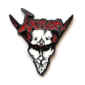 Puede incluir: Un pin de esmalte metálico con la palabra Venom en una fuente estilizada roja y negra. Debajo del texto hay una ilustración de una cabeza de cabra blanca con ojos rojos y un pequeño pentagrama rojo en la frente, delineado en metal negro.