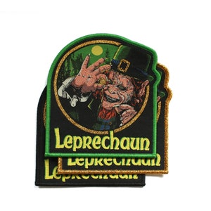 Puede incluir: Parche bordado con un leprechaun de pelo rojo, sombrero verde y moneda de oro. El parche tiene un fondo negro con la palabra "Leprechaun" en verde. El parche es rectangular con la parte superior redondeada y un borde dorado brillante.