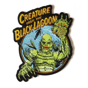 May include: An embroidered patch featuring the Creature from the Black Lagoon in shades of green with orange lips. The design includes a blue circular background, a small silhouette of a swimmer, and the text CREATURE FROM THE BLACK LAGOON.