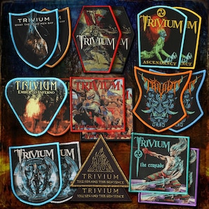 May include: A collection of embroidered patches featuring the band name "Trivium" and various album art designs. The patches are in various shapes, including shields, triangles, and hexagons, with vibrant colors and detailed imagery. Some patches include text like "What the Dead Men Say" and "Ascendancy".