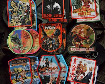 May include: A collection of rectangular, circular, and shield-shaped embroidered patches featuring various movie poster graphics, including titles like Tales from the Crapper, Blood Junkie, The Toxic Avenger Part III, Monster in the Closet, and Christmas Evil.