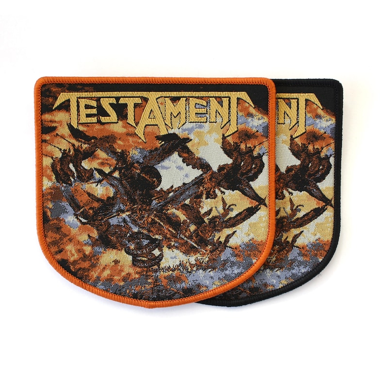 May include: Two rectangular fabric patches with rounded bottom corners featuring the word TESTAMENT in gold lettering. The design displays a dark, chaotic scene with orange, brown, and blue tones. One patch has an orange border, the other black.
