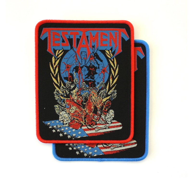 May include: Two rectangular embroidered patches featuring the Testament band logo in blue and red. The design includes a globe, a laurel wreath, and a graphic of figures over an American flag. One patch has a red border, the other a blue border.