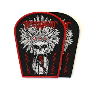 May include: Two shield-shaped embroidered patches with a black background and red border. The design features a white skull wearing a feathered headdress, the word TESTAMENT in red, and the red text NATIVE PRIDE flanking the central graphic.