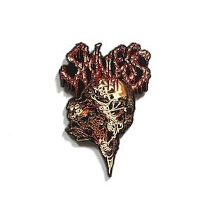 May include: A black metal pin with a red and gold design. The pin features the word "SINNER" in a dripping font and a skull with a detailed design.