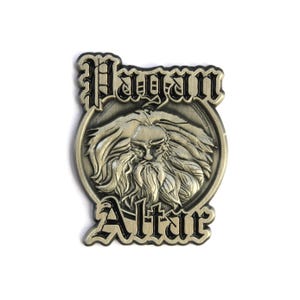 Pode incluir: Um alfinete de metal dourado com contorno preto. O alfinete apresenta um design circular com o rosto de um homem barbudo no centro. As palavras "Pagan Altar" estão escritas em uma fonte gótica acima e abaixo da imagem.