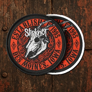 Könnte beinhalten: Zwei runde schwarze Aufnäher mit roten und weißen Designs. Die Aufnäher zeigen den Text "ESTABLISHED 1995 DES MOINES, IOWA" am Rand. Das zentrale Design zeigt einen Ziegenschädel und den Bandnamen "Slipknot".